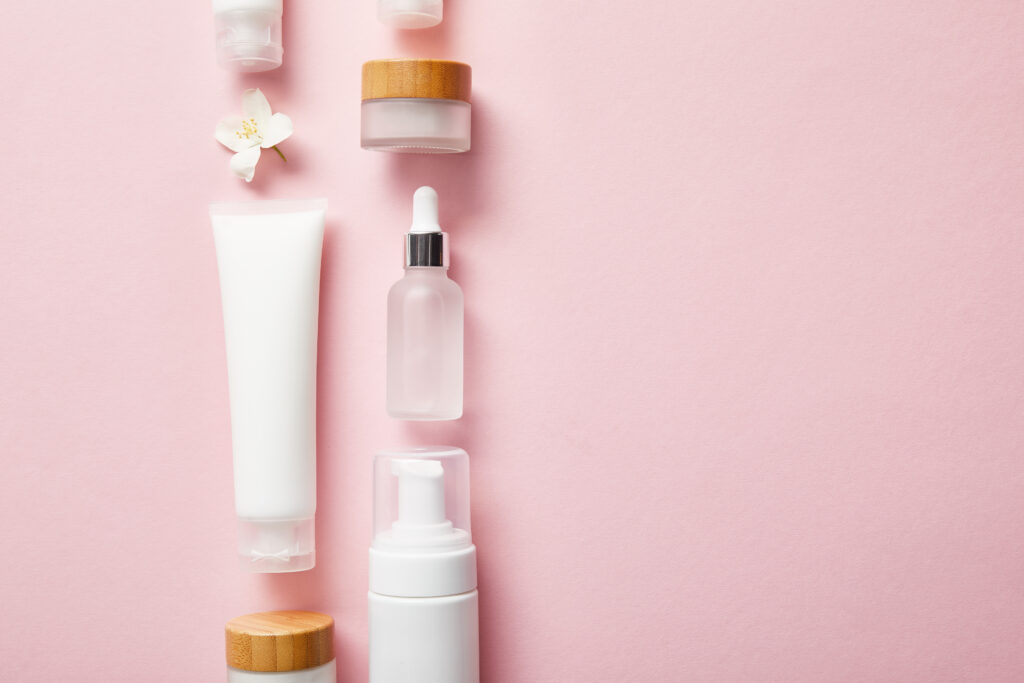 flat lay of different cosmetic containers and jasmine flower on pink