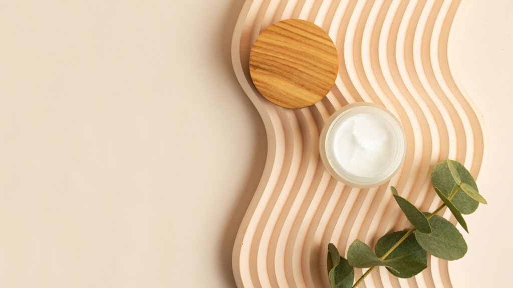 open skin care packaging with white cream inside.wooden cover near it. box lying on the wavy podium.pastel colors,good as mockup,large banner.