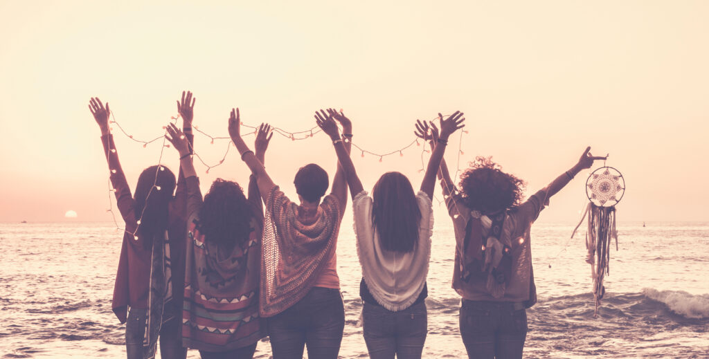 vintage tones pictures of five women friends viewed from rear giving up hands for happiness in front ona sunset on the ocean and holding lights and a dreamcatcher for spiritual concept