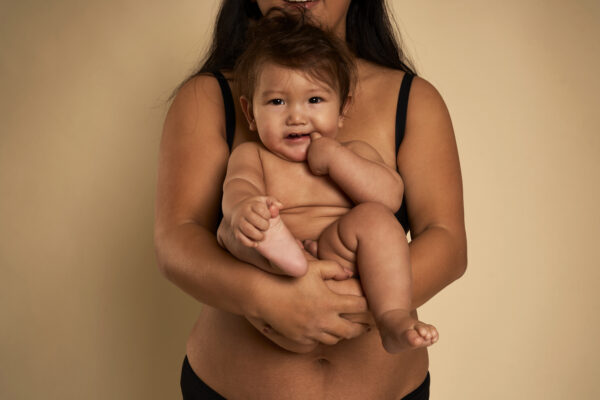 portrait of cheerful asian toddler carried by unrecognizable mother
