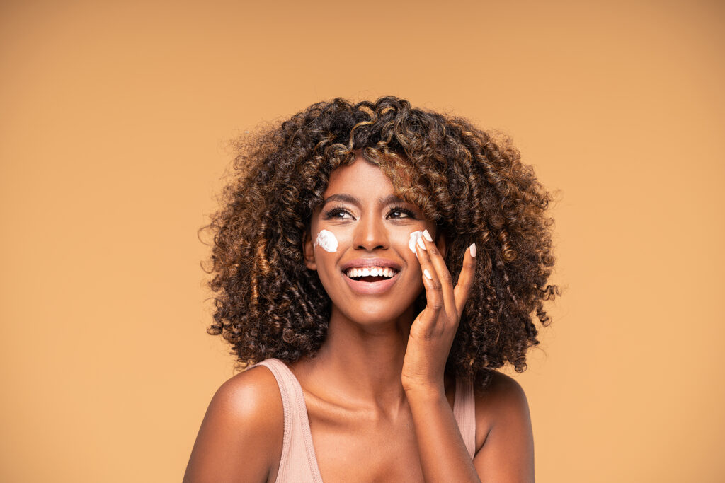 beautiful african girl applying a cream on cheek.
