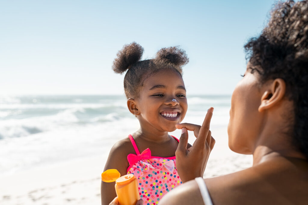 lovely black mother applying sunscreen on cute little black girl