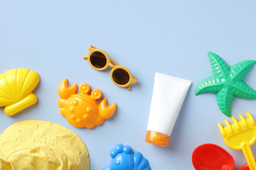 flat lay baby sunscreen tube, sunglasses, sand molds and panama hat on blue background.