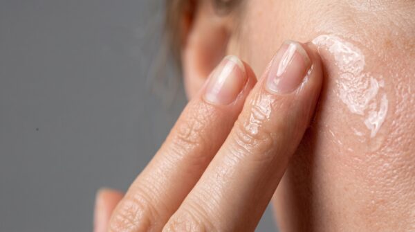close up of fingers applying clear gel serum to facial skin for skincare