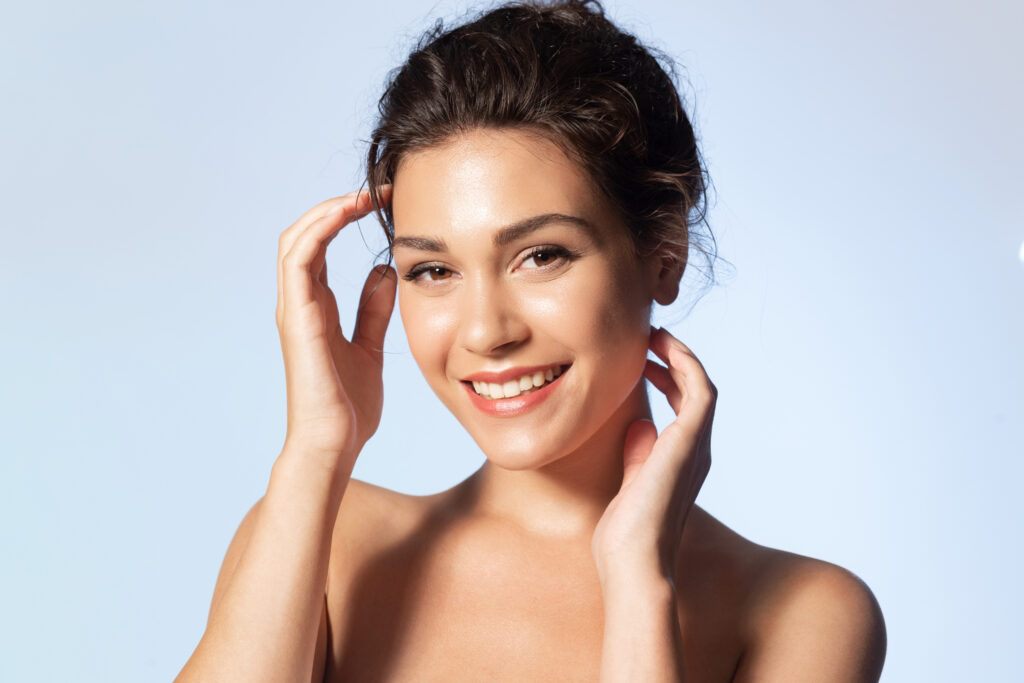 smiling young girl with naked shoulders touch perfect smooth face skin. natural woman beauty and skincare concept