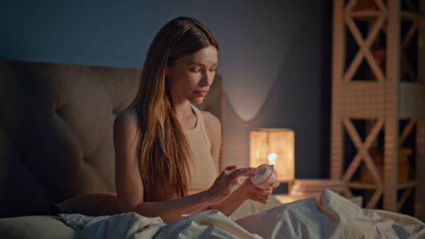 woman applying moisturizer cream on face preparing to sleep in cozy apartment