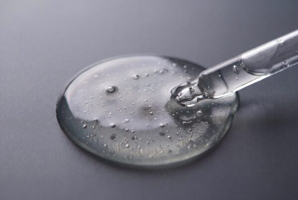clear cosmetic serum drop from glass pipette on dark background with texture and bubbles